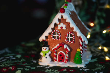 Gingerbread house Christmas decoration with a snowman and Christmas Tree with festive lights in the backgroundの写真素材