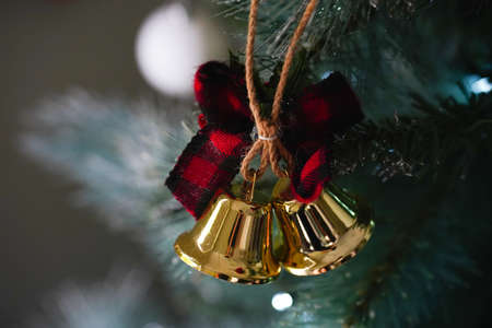 A Christmas decoration with two golden bells and a red ribbon hanging on a Christmas treeの写真素材
