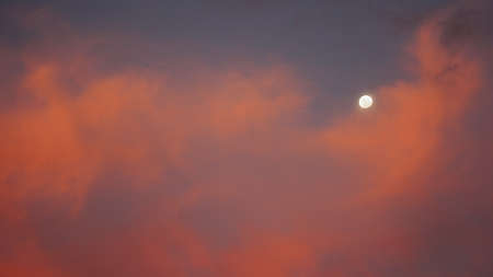 The moon behind colourful clouds at duskの写真素材