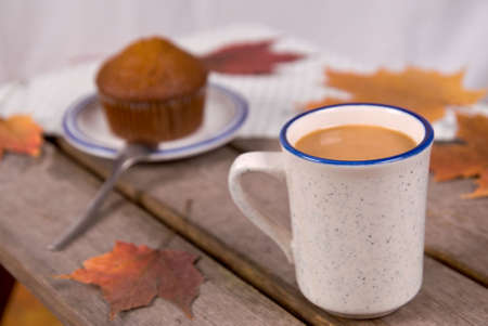Cup of Coffee and a bran muffin on a picnic table with fall leavesの写真素材