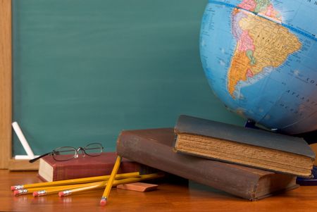 Old school books on a desk with a globe in front of a green chalkboard