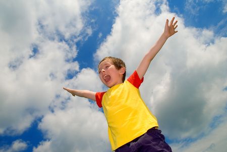 Boy with his arms wide open in front of a sky with cloudsの写真素材