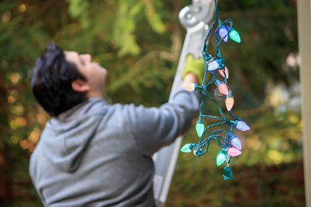 young man in gray climbing a ladder to decorate for christmas