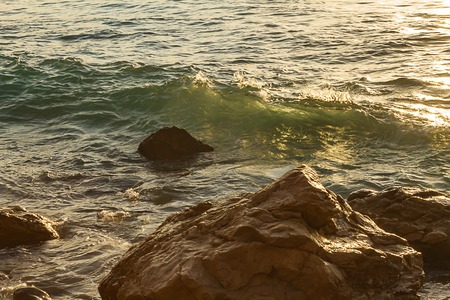curling wave forming with transparent green and yellow light moving towards rocksの写真素材