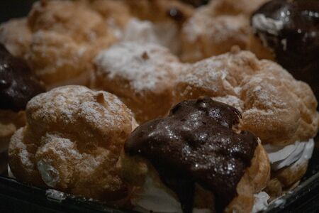 powdered sugar and shiny chocolate glased cream puffs filled with a swirl of white cream