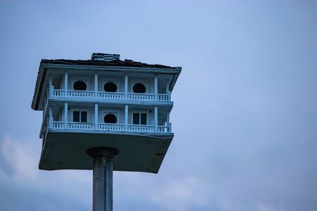 an old birdhouse with pilars a wrap around deck and roof on a metal pole
