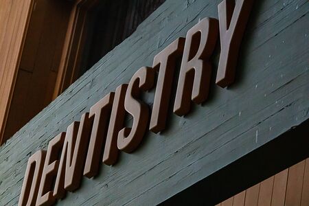 letters hung on large wooden beam spelling dentistry with reflections and shadowsの写真素材