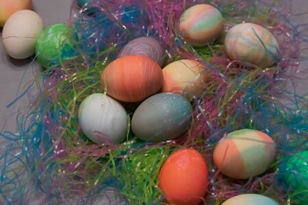 dyed easter eggs gathered together on a table with colorful plastic easter grass