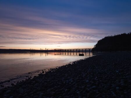 sunset glowing over a dock leading out to water of puget sound in summer afternoon