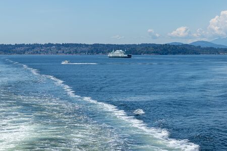 wake in water from boat with washington state ferry in the background in spring