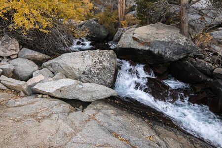 rushing water seen from hiking trail with boulders and autumn colorsの写真素材