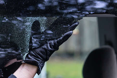 shattered glass of a car window being romoved with a black gloveの写真素材