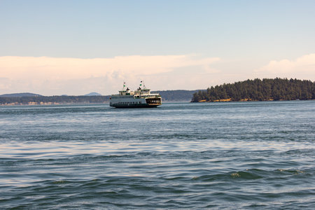 Ferry Sailing Across Sunlit Coastal Waters Toward Forested Islandの写真素材