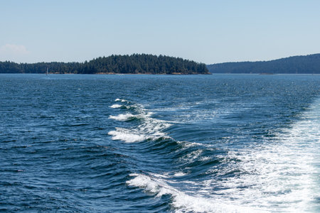 ferry Boat Crossing Deep Blue Channel Toward Forested Islandsの写真素材