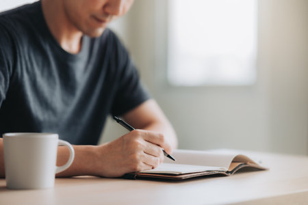 Making some notes. Close-up part of young man writing in notebook while sitting at he working placeの写真素材