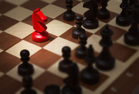 Chessman red horse surrounded by black on the chessboardの写真素材