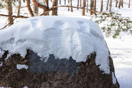 An imprint of a silhouette of a man in the snow on a large stone in a winter park.