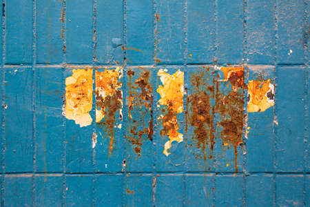 Cracked oil paint on tile surface background. Dirty blue cracked paint with peeling pieces, and under it is a white tile with orange rusty streaks from waterの写真素材