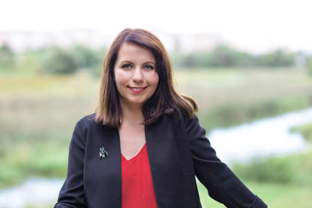 Portrait of woman in red dress and black jacket, city park with river on blurred backgroundの写真素材