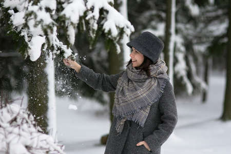 Portrait of a woman in warm fashionable clothes in a snowy winter park. She smiles and enjoys the...