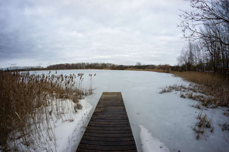 Wooden pier on a frozen winter lake. Deserted cold calm winter landscape.の写真素材