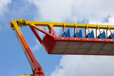 Deserted colorful red and yellow amusement park amusement ride against the backdrop of a cloudy blue sky.の写真素材