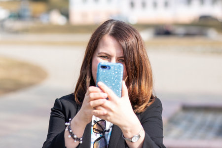 Beautiful woman in a black jacket takes a selfie. The woman has beautiful brown hair and holds a...