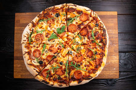 Colorful appetizing fresh hot pizza with salami and oregano cut into slices on an oak board against a dark wood table backgroundの写真素材
