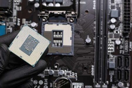 Central processing unit (central processing unit) in a man's hand in a black glove - close-up, with a blurred motherboard in the background.の写真素材