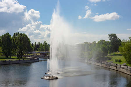 A large fountain with high jets of water in the middle of the river in a city park in bright sunny weatherの写真素材