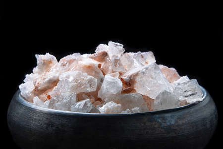 Large chunks of pink himalayan salt in black handmade earthenware bowl isolated on black backgroundの写真素材