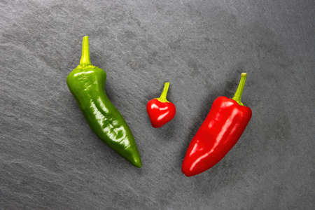Red and green hot chili peppers on a gray stone background. In the middle, a small red pepper in a heart shapeの写真素材