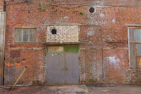 A large old dilapidated house of red and white brick with rusted windows and metal gates. Old dirty abandoned factory building.の写真素材