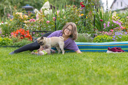A girl with glasses plays with a pug puppy on the lawn in a summer blooming gardenの写真素材