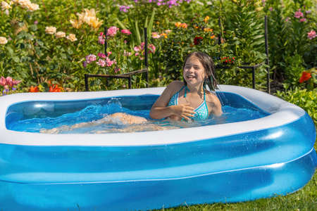 A girl in a blue swimsuit bathes in a blue inflatable pool in a blooming gardenの写真素材
