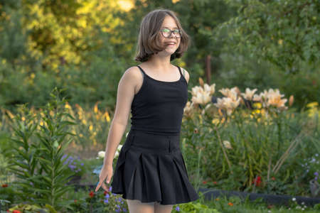 Girl with glasses in black clothes laughs in a blooming summer gardenの写真素材