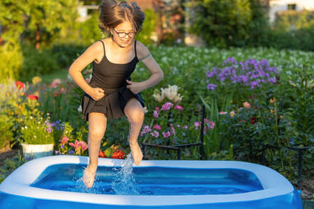 A girl with beautiful multi-colored hair in glasses jumps in cool water in an inflatable pool in an evening hot summer gardenの写真素材