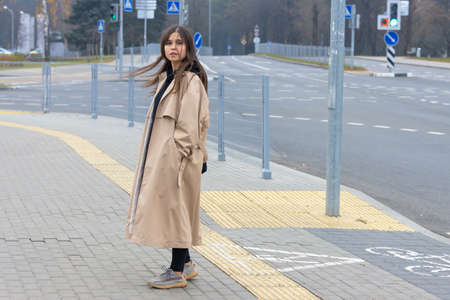 A beautiful girl in a long coat stands on a deserted city streetの写真素材