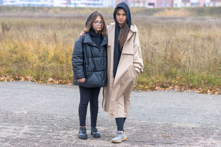 Two girls in autumn clothes stand together on a deserted outskirts of the cityの写真素材