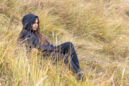 A beautiful girl with long hair in black clothes lies on a hillside among the thick autumn grassの写真素材
