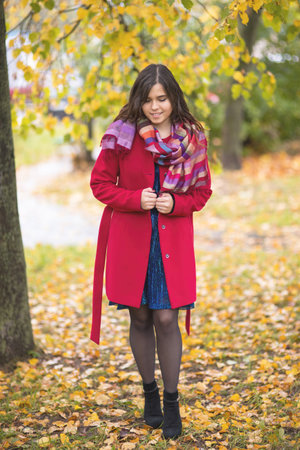 Young beautiful girl in a red coat stands in an autumn park among yellow leavesの写真素材