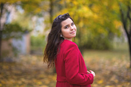 Young beautiful girl in a red coat stands in an autumn park among yellow leavesの写真素材