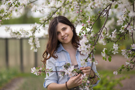 A young beautiful girl stands among the branches of a blossoming apple tree in a spring gardenの写真素材