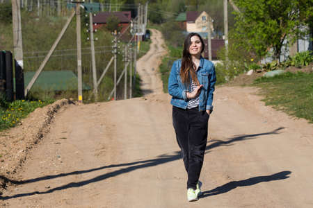 Young cheerful girl walking along a dirt country road on a sunny summer dayの写真素材