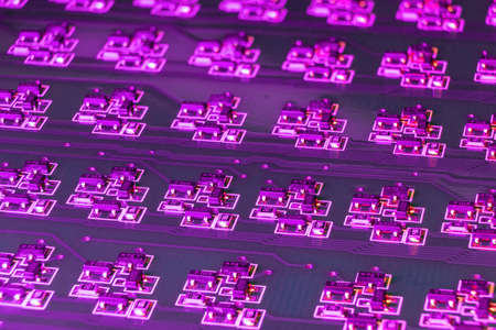 Close-up of an electronic circuit board with many SMD components illuminated by ultraviolet light....