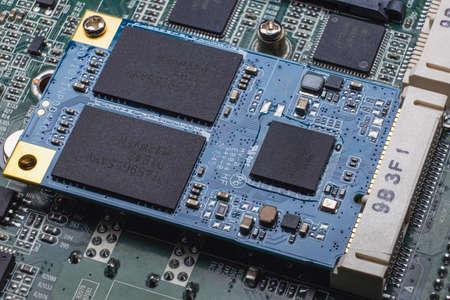 An M.2 format SSD module installed in a slot on the computer's motherboard. Close-up of an electronic circuit board with memory chips and SMD componentsの写真素材