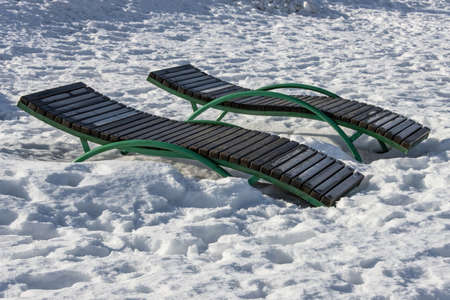 A pair of sun loungers on a snow-covered beach waiting for the warm season and tourists.