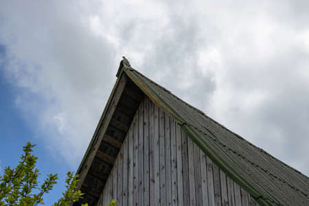 The old pointed roof of a village house with a singing bird sitting on it against a cloudy sky.の写真素材