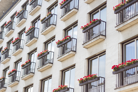 Building hotel facade balconies with red flowers on the railing viewed from belowの写真素材