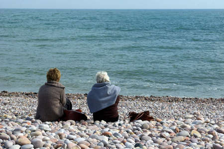Senior ladies sitting on a pebble beach in Devon, with a view on the seaの写真素材
